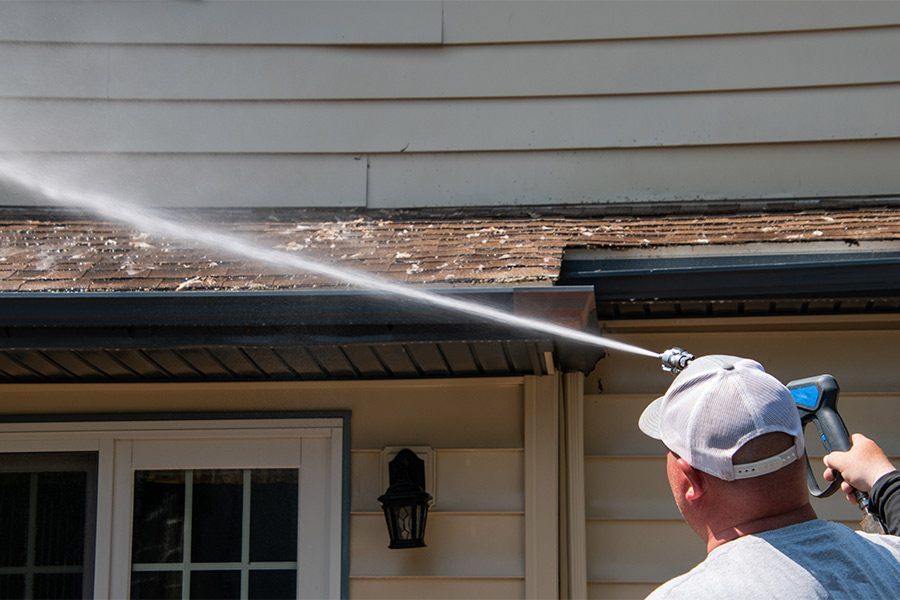 man pressure washing shingle