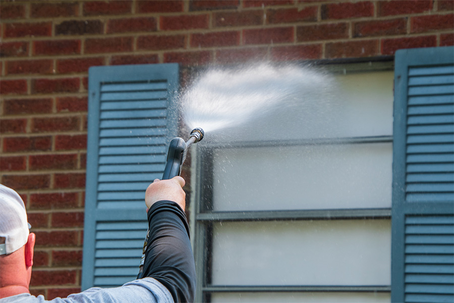 man pressure washing window
